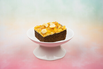 Toffee chocolate cake slice on high plate on colorful background with macadamia seeds at above for dessert break