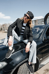 A young, beautiful girl is sitting on the hood of a car.