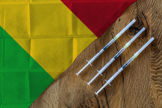 Concept of the ongoing efforts by Mali to deliver and distribute COVID-19 vaccines with three syringes on a wooden table ready to use with a Malien Flag. Copy Space for Text and Graphics.