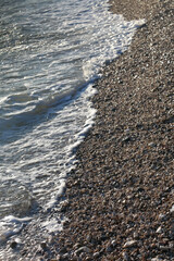 Pebbles and water on a beach, illuminated by golden hour light. Selective focus.