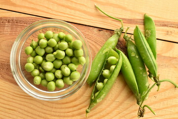Several ripe organic, green peas pods on a wooden table with a glass saucer, close-up, top view.