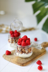 Granola with greek yogurt and raspberries in glass jar on rustic wooden board.