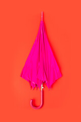 Pink folded umbrella on red background. Nobody
