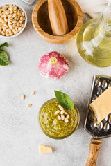 Pesto sauce in a jar with a piece of parmesan cheese, basil leaves, pine nuts and olive oil in a bottle. Copy space.