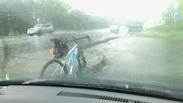 Heavy rainy road with bicycle standing on roadside through wind-screen in car 