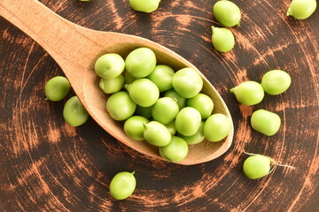 Several ripe organic, green peas with a wooden spoon on a clay plate, close-up, top view.