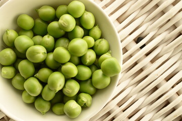 Several ripe organic, green peas in a white saucer on a tray of vines, close-up, top view.