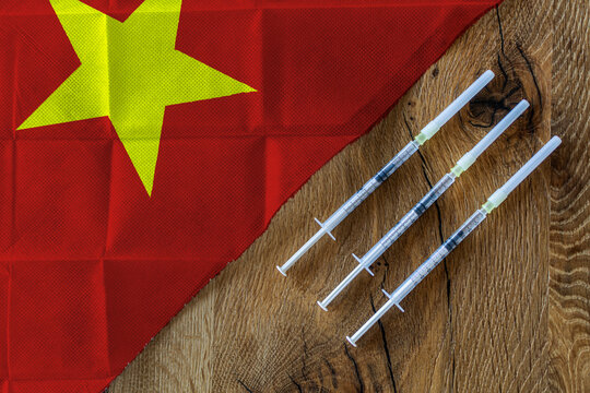 Concept of the ongoing efforts by Vietnam to deliver and distribute COVID-19 vaccines with three syringes on a wooden table ready to use with a Vietnamese Flag. Copy Space for Text and Graphics.