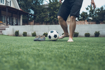 Obraz premium Legs of soccer player training at home kicking the ball without shoes on green grass in garden