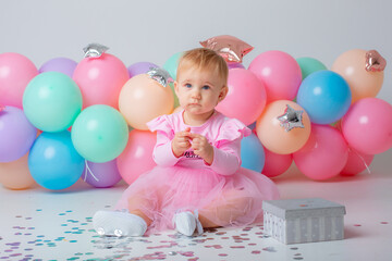 Fototapeta na wymiar baby girl celebrates birthday on white background catching confetti balloons