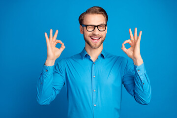 Photo of young man happy positive smile blink eye show okay alright great decision advert isolated over blue color background