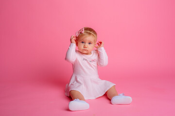 cute little baby girl in pink summer dress sitting on pink background