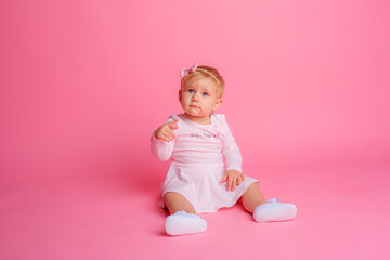 cute little baby girl in pink summer dress sitting on pink background