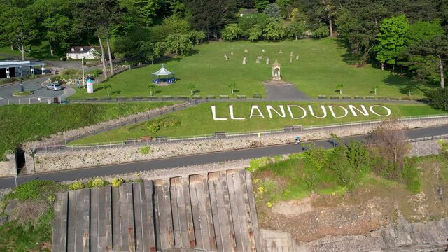 Cyclist rides part the Llandudno sign in front of the park