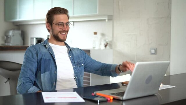 young business man sits at table with a laptop working in home office. He gets great news and is delighted. clicks fingers and says yes