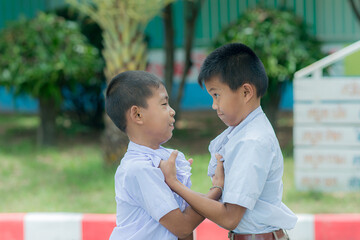 Two Asian schoolboys facing each other getting bullied Children fighting with classmates in the school park.