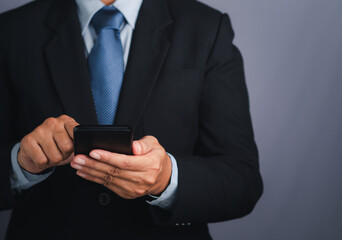 Businessman using a smartphone while standing with a gray background. Space for text. Communication and technology concept
