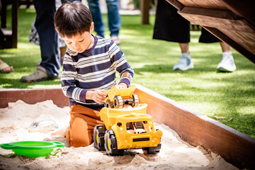 Asian child boy playing toy and sand in sandbox with natural background. Copy space.