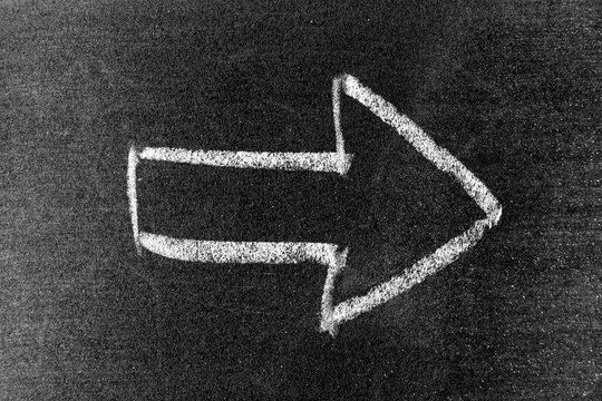 White color chalk hand drawing in arrow shape on blackboard or chalkboard background