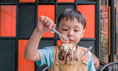 Little asian boy eating ice cream at an intdoor cafe. Copy space.
