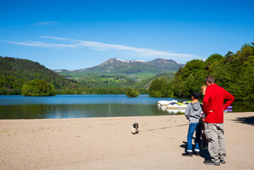 Fototapeta na wymiar Family (unrecognizable; back view) with dog admiring Chambon lake in Auvergne Volcanic Regional Nature Park. Puy-de-Dome, Auvergne, France. French tourism background. Travel, happy together concepts.