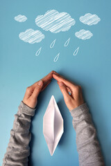 Hands protect the paper boat from bad weather. A symbol of protection of life and an easy way in...