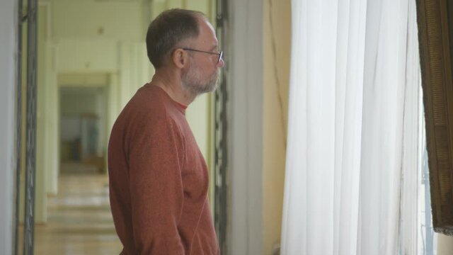 The man in the gallery standing at the window considering artwork.