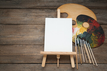 Easel with blank canvas, brushes and palettes on wooden table, flat lay. Space for text