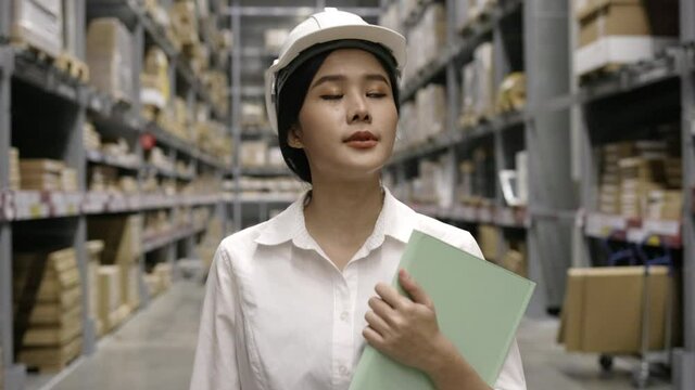 Young asian Woman officer check products in warehouse of modern factory. Work Evaluate items in shelves store. Online delivery service. Workers take notes in note paper. Freight business. 