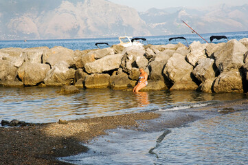 Caucasian woman sitting on a rock of the breakwater in the afternoon. with the Policastro gulf in the background. Scario, Italy. 