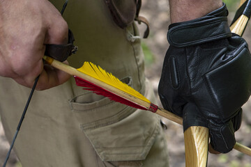 A rough man's gloved hand holds a bow and aims an arrow, close-up, selective focus. Concept: men's hobbies, survival in difficult conditions, hunting and recreation.