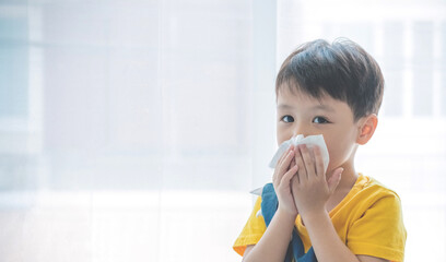 Little boy blowing nose into tissue paper and wearing surgical face mask. Copy space. - Powered by Adobe