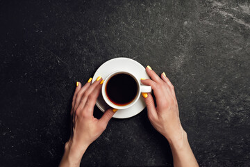 Woman holds cup with coffee on black background top view