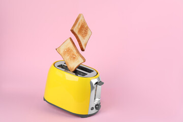 Bread slices popping up from modern toaster on pink background. Space for text