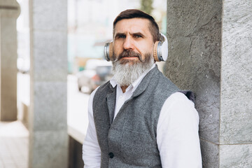 Obraz premium Bearded gray-haired senior man listening to music on the clean urban spaces