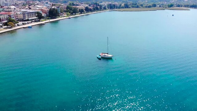 A boat on blue lake of Ohrid, North Macedonia. Sun light is glittering on water surface. Peaceful moment of travel or trip. Beautiful scenic took with aerial drone 4K 30fps.