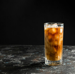Cold coffee with ice and cream in a tall glass on a black background.