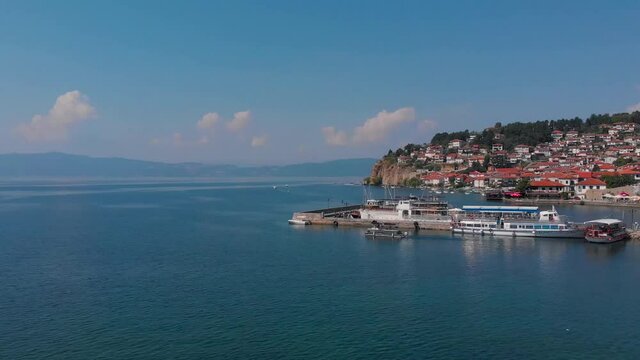 A huge lake of Ohrid, North Macedonia. Historic Medieval houses with red roofs are on the shore of blue water. Birds are swimming on surface. Beautiful scenic took with aerial drone 4K 30fps.