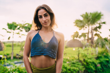 Half length portrait of young Caucasian tourist dressed in stylish knitted top looking at camera during leisure time at nature, beautiful woman with brunette hair posing during sunny summer day