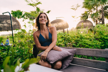 Half length portrait of cheerful girl smiling at camera during leisure weekend at home courtyard,...