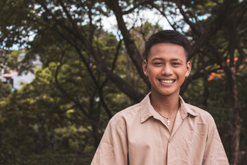 A young smiling Filipino man at the park. Dark complexion and wearing a light brown polo shirt.