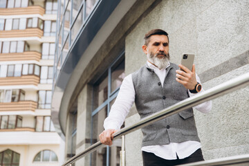 A bearded gray-haired senior man uses and talks on a smartphone