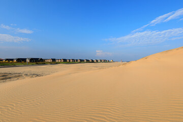 Wooden houses and sand dunes against a blue sky background