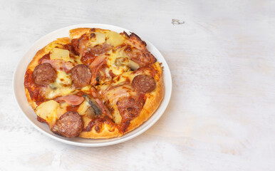 Close up  pizza topped bacon, pineapple, and cheese on white wooden table.