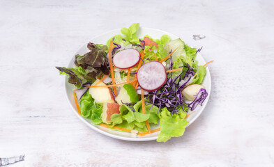 Close up vegan salad, fresh green leaves mix and vegetables and fruits on the white wooden table, healthy food.