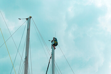 Sailor on top of sailing boat mast doing maintenance or radar system, mast harness human lifting...