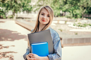 Caucasian student girl walking in the park and holding notebook folders in her hands Education,...