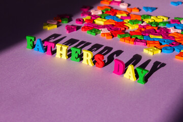 Child's toy letters spelling Fathers Day with a large shadow next to randomly lying letters on purple background.