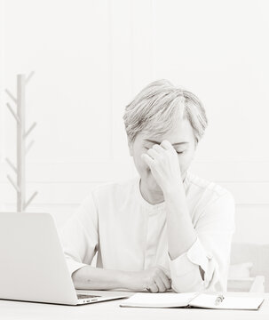 Senior Asian Woman Holding Head With Hands While Sitting And Working With A Laptop At Home.