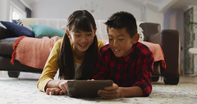 Asian brother and sister smiling and using tablet at home